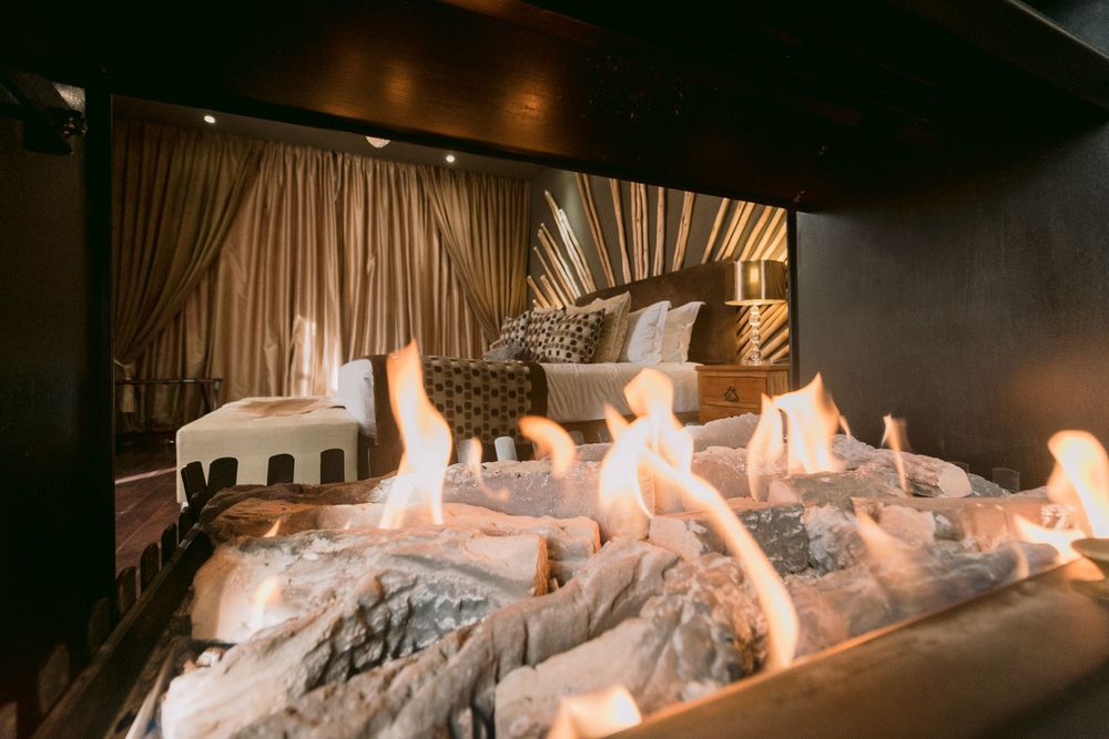 Cozy luxury bedroom viewed through a glowing fireplace with fur blanket in the foreground.