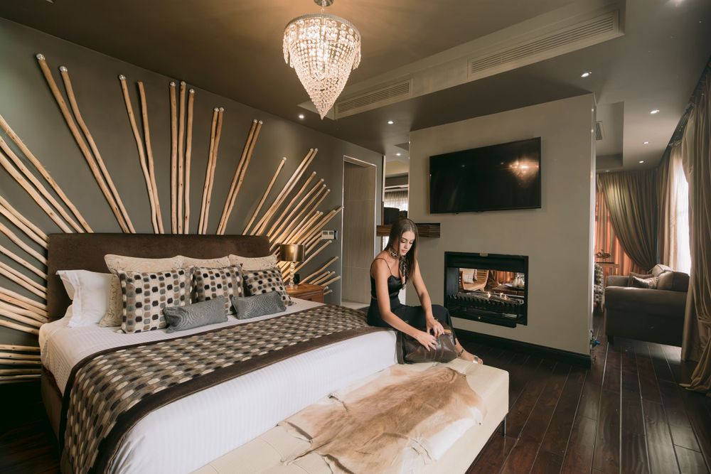 Stylish hotel suite with sunburst wall decor, fireplace, crystal chandelier and woman making bed.