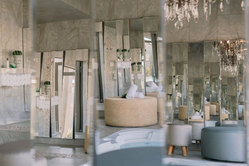 Elegant spa interior featuring mirrored walls, a round ottoman, and crystal chandeliers.