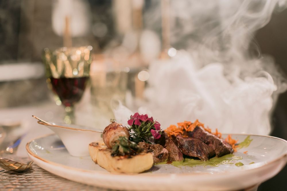 Elegant fine dining dish with meat and vegetables served with dramatic smoke effect on white plate.