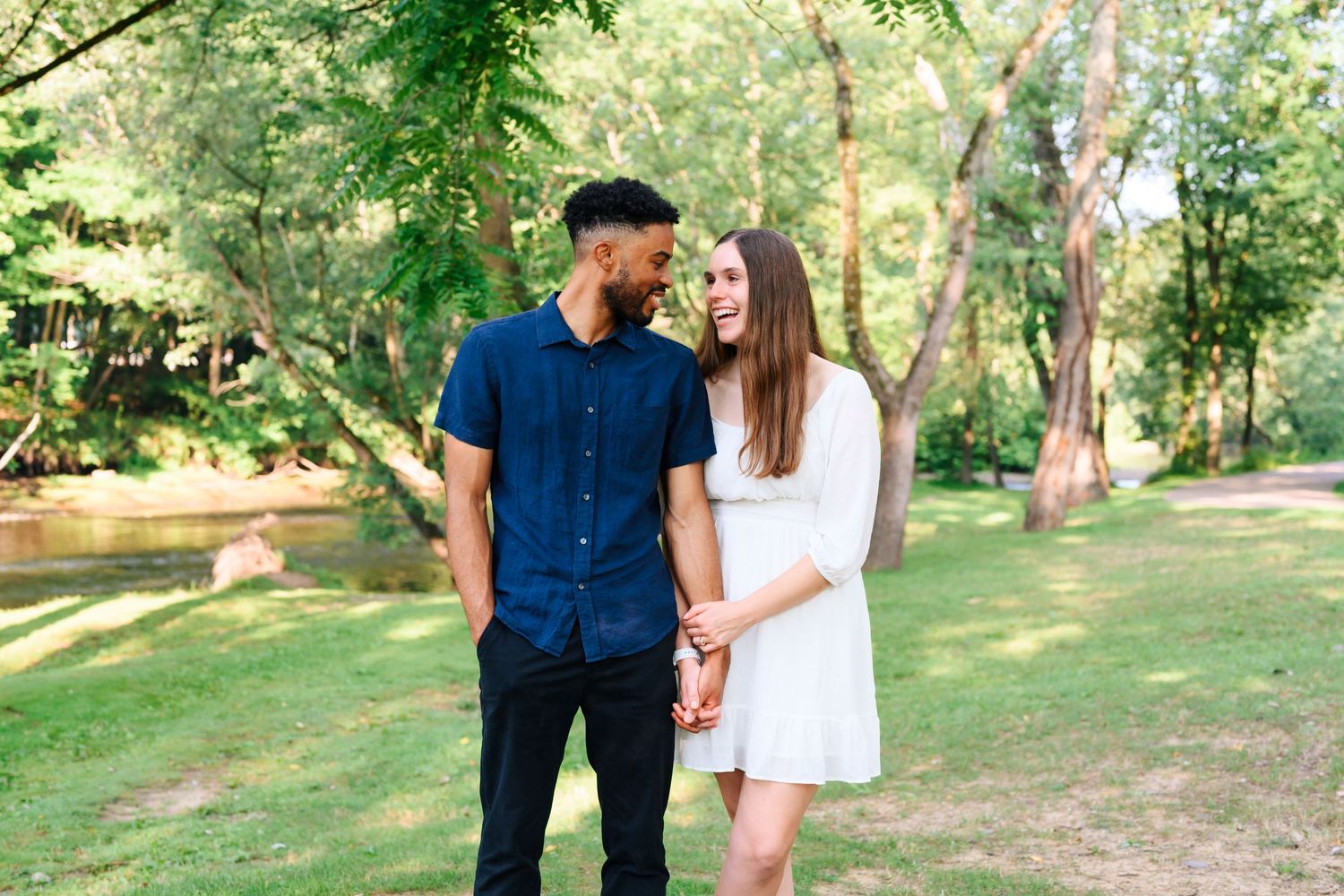 Couple holding hands in a sunny park with vibrant green foliage.