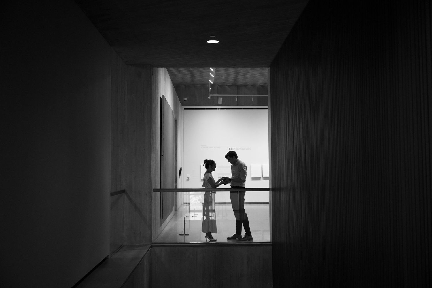 A silhouette of figures in a dark hospital hallway, viewed through a corridor with handrails.