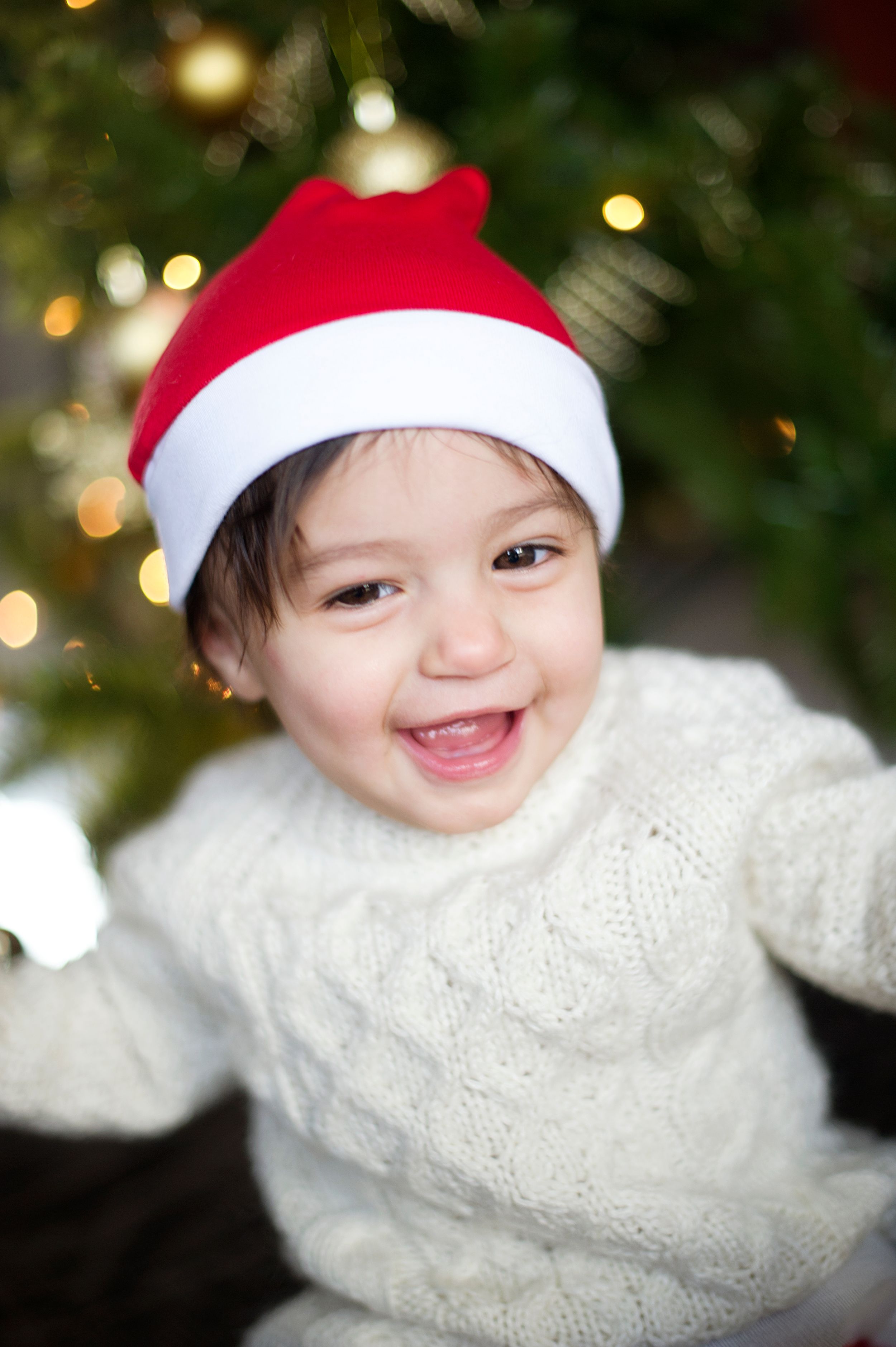 Infant smiling in a cozy sweater and Santa hat by a Christmas Tree, captured by Phoebe Lee Photo in Toronto