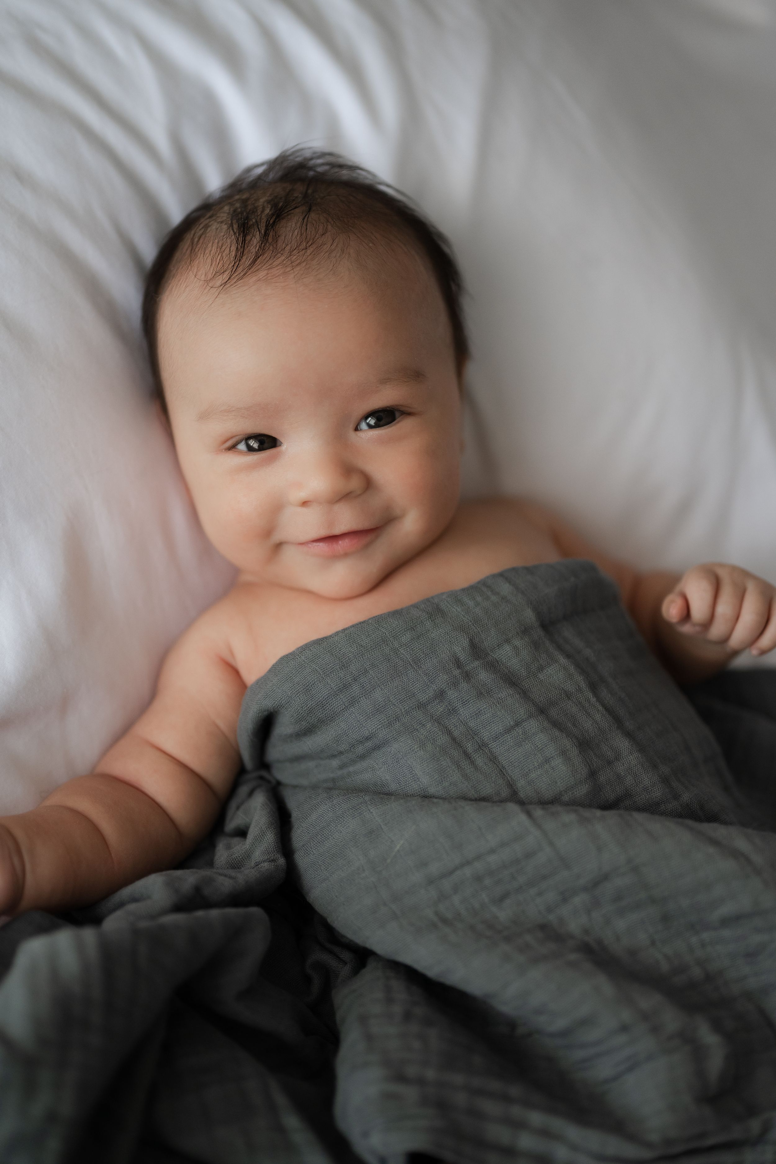 Baby boy smiling under a gray blanket, captured by Phoebe Lee Photo during an in-home baby session in Toronto