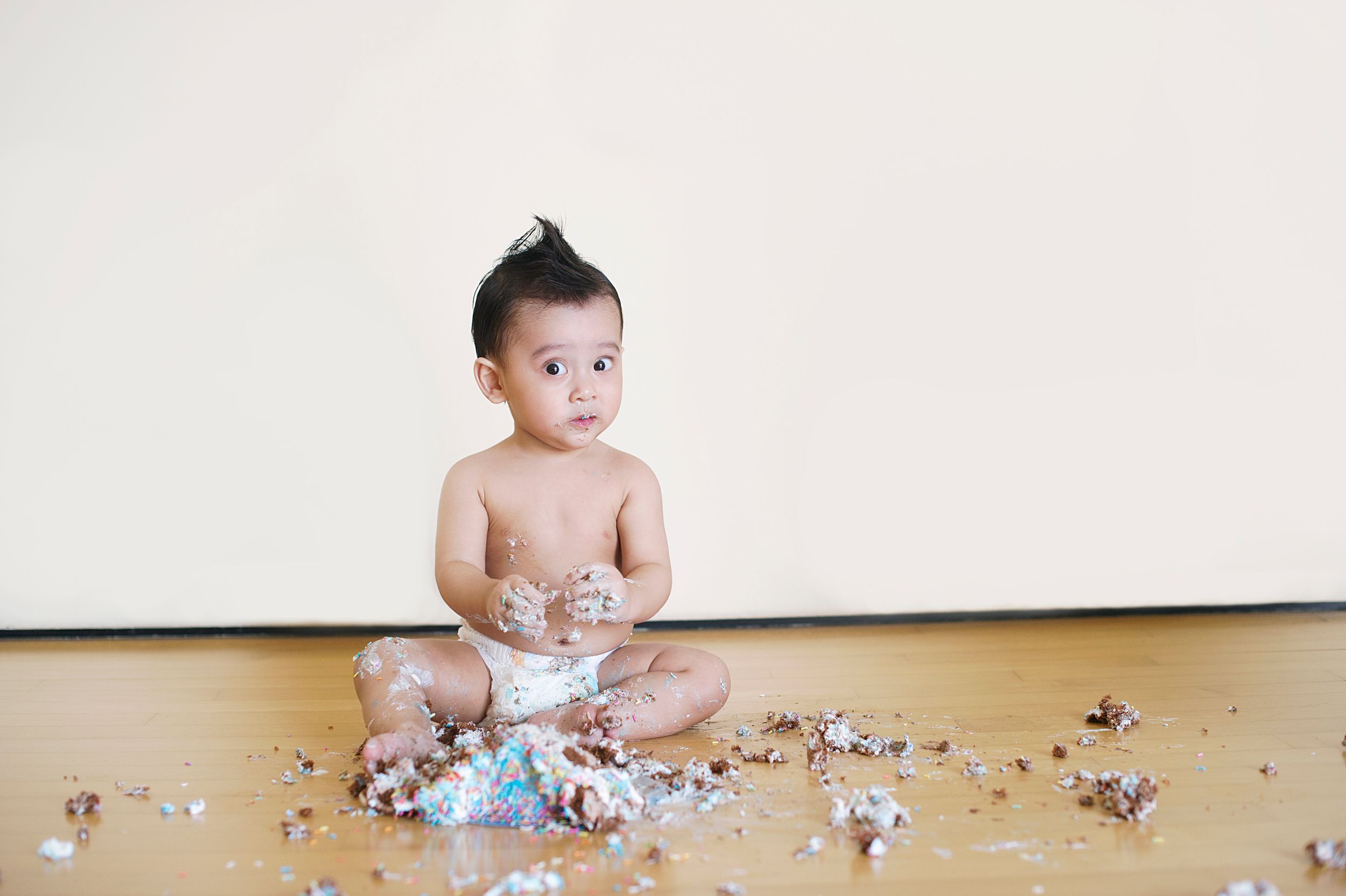 Toddler enjoying a cake smash session on a wooden floor, photographed by Phoebe Lee Photo in Toronto