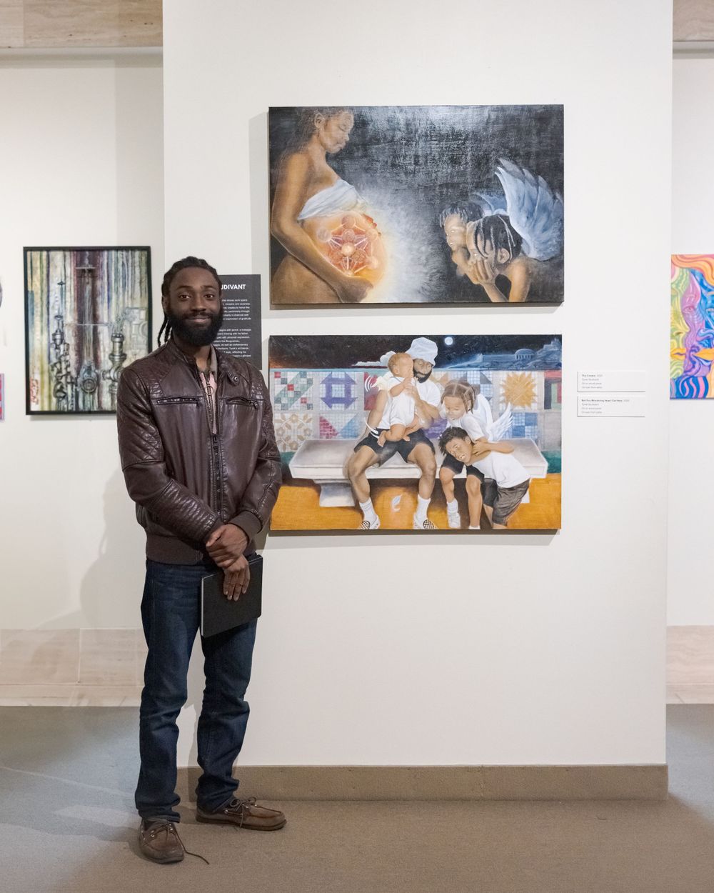 Man in leather jacket standing before figurative paintings in a contemporary art gallery.