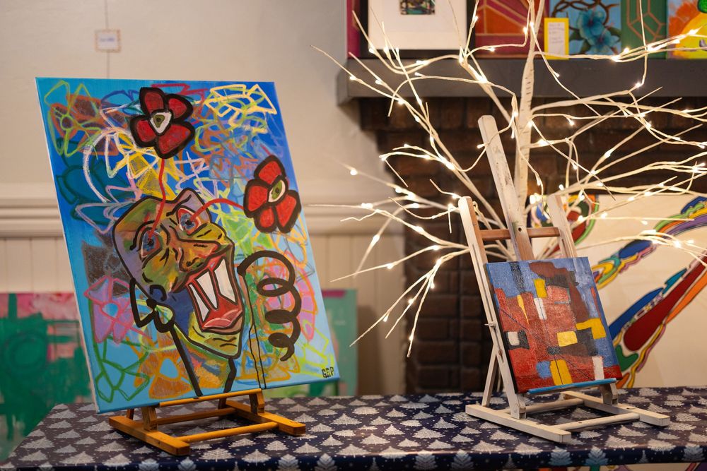 Colorful abstract artwork displayed on an easel beside a decorative illuminated white tree.
