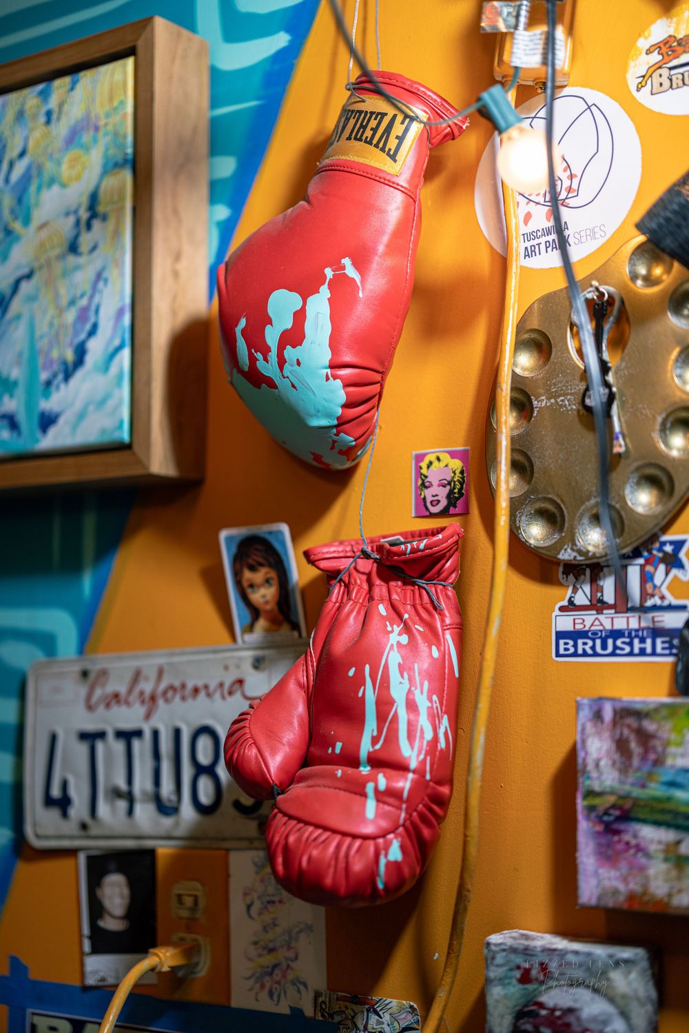 Red Everlast boxing gloves with paint splatter hanging on colorful art studio wall.