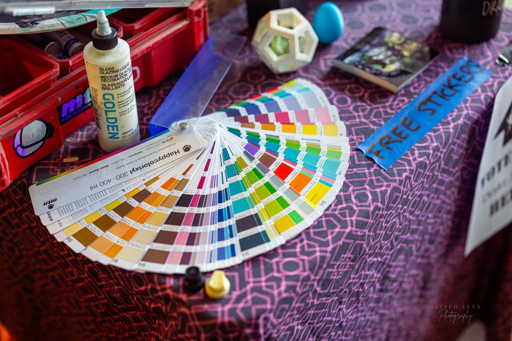 Colorful Pantone color swatch fan displayed on a purple patterned table with art supplies.
