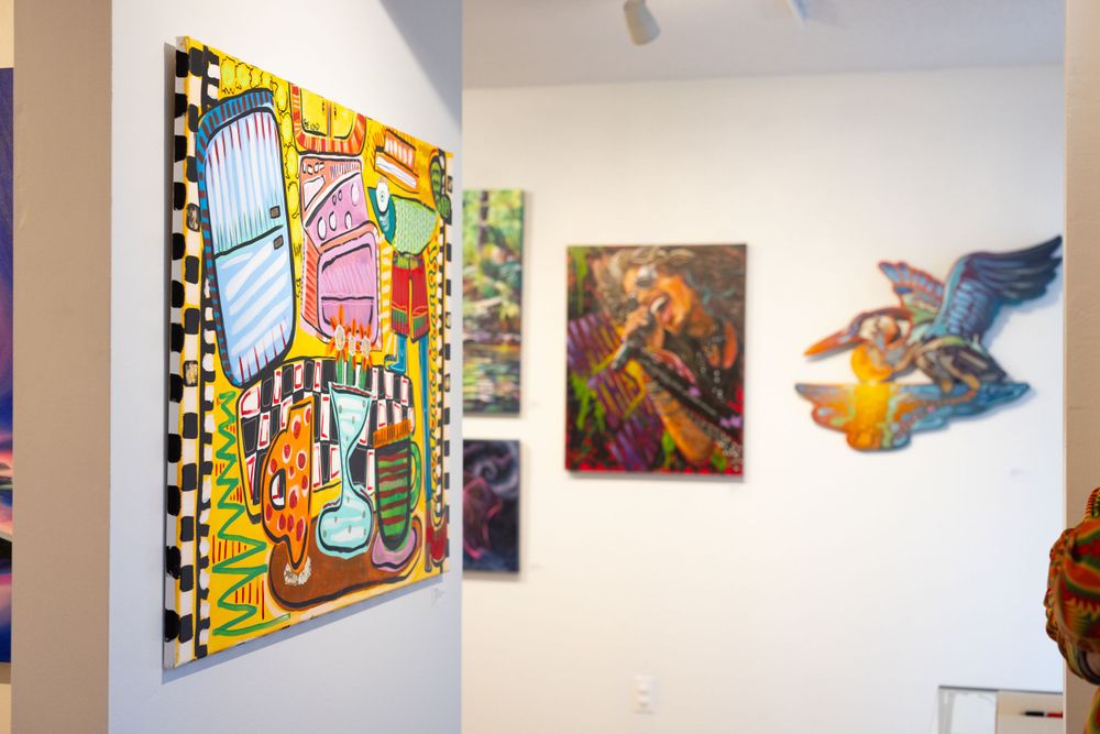 Gallery wall displaying vibrant pop art paintings including a checkered kitchen scene and a bird sculpture.