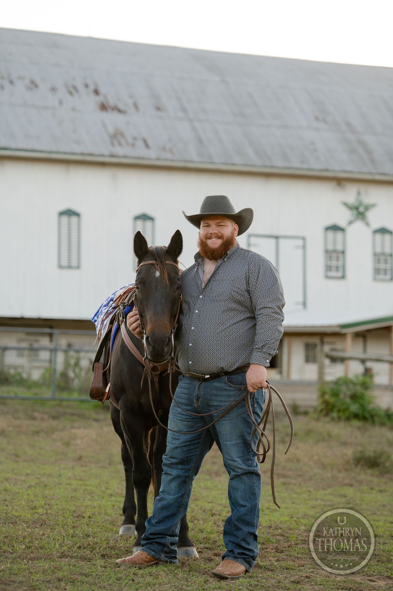 Dark horse with western tack stands with handler by white barn building.