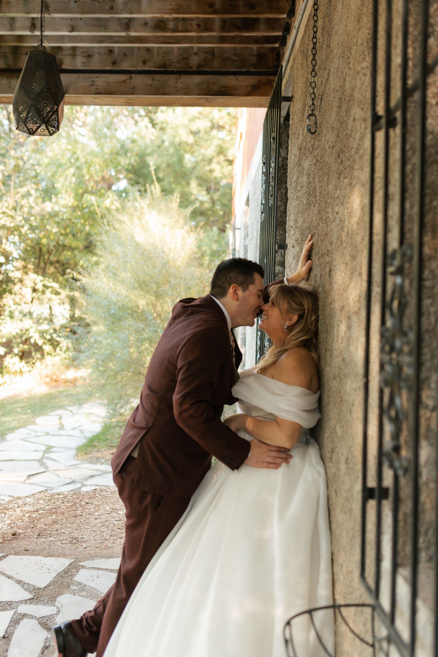 Bride and groom sharing romantic kiss against stone wall at outdoor wedding venue.