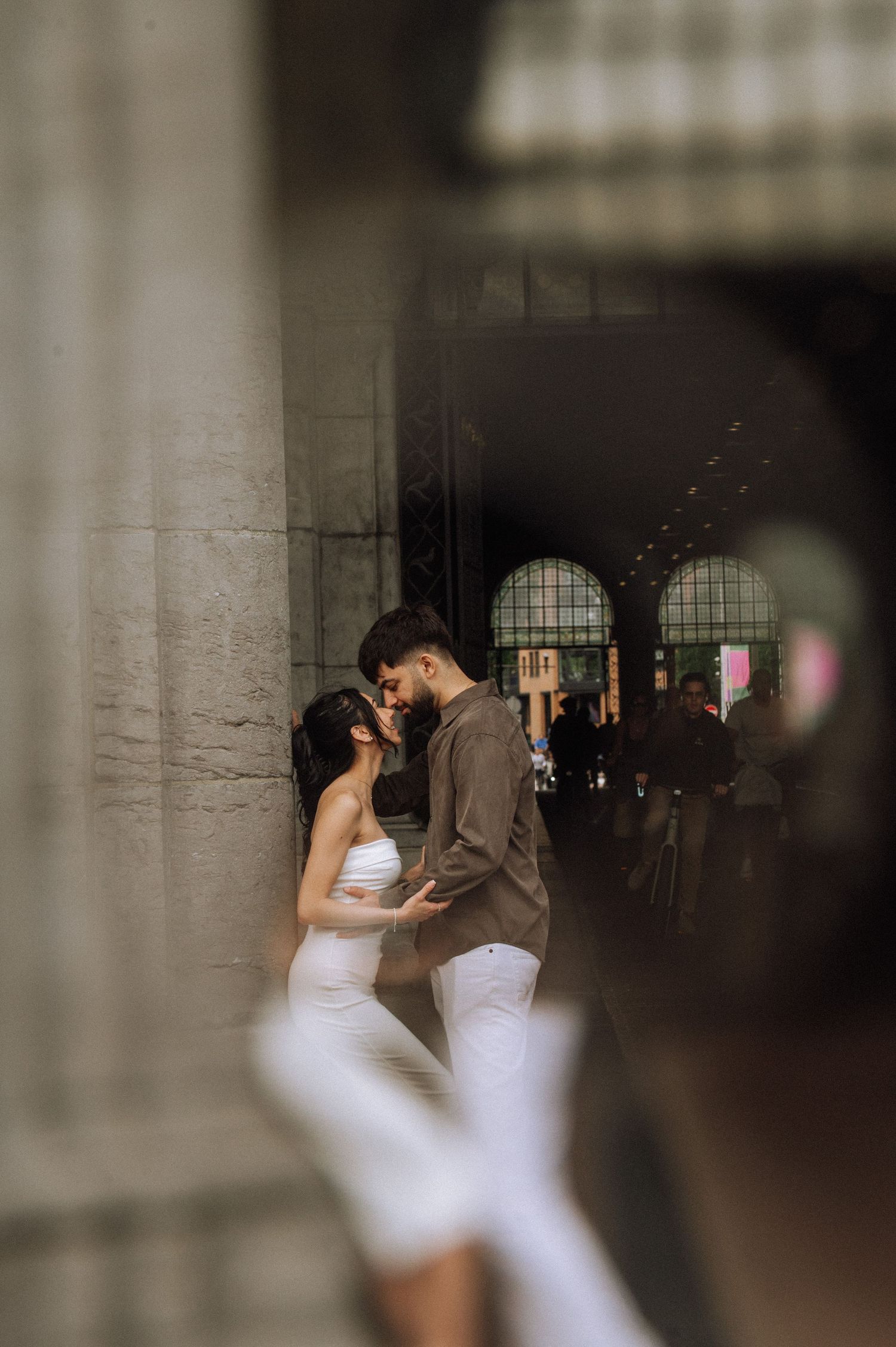 Couple in white and olive shirt share a romantic kiss between stone columns, Rijksmuseum, Amsterdam.