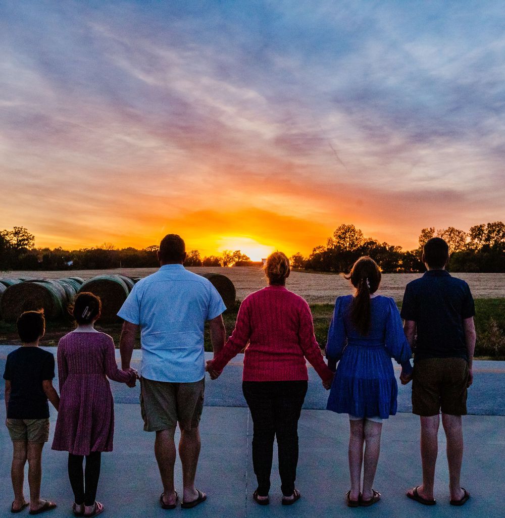A family silhouetted against a vibrant orange sunset sky while watching together from a walkway.