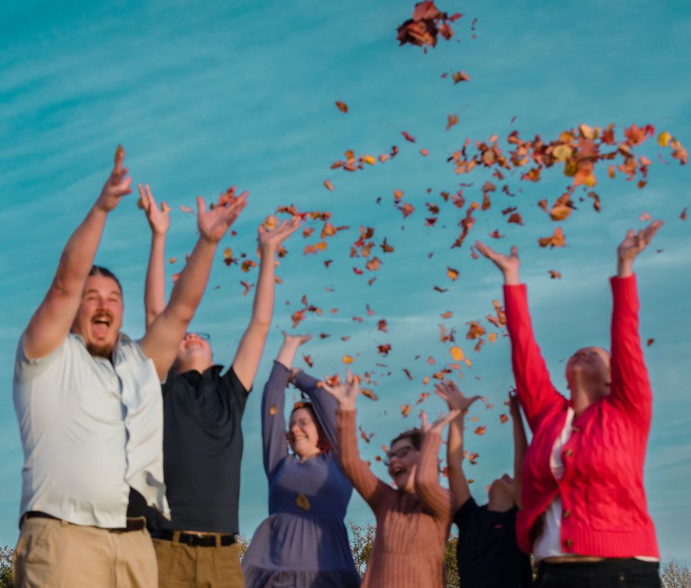 A group of people joyfully toss red petals into a bright turquoise sky during an outdoor celebration.