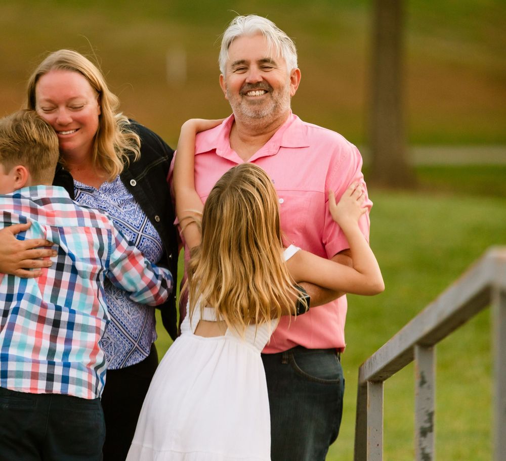 A family sharing a joyful moment together outdoors on wooden steps during a sunny day.