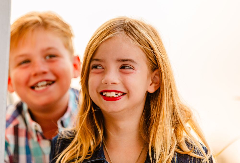 Two joyful children with bright smiles share a candid laughing moment together in natural light.