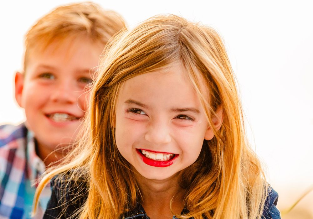 Two happy children smiling and laughing together outdoors with bright natural lighting in the background.