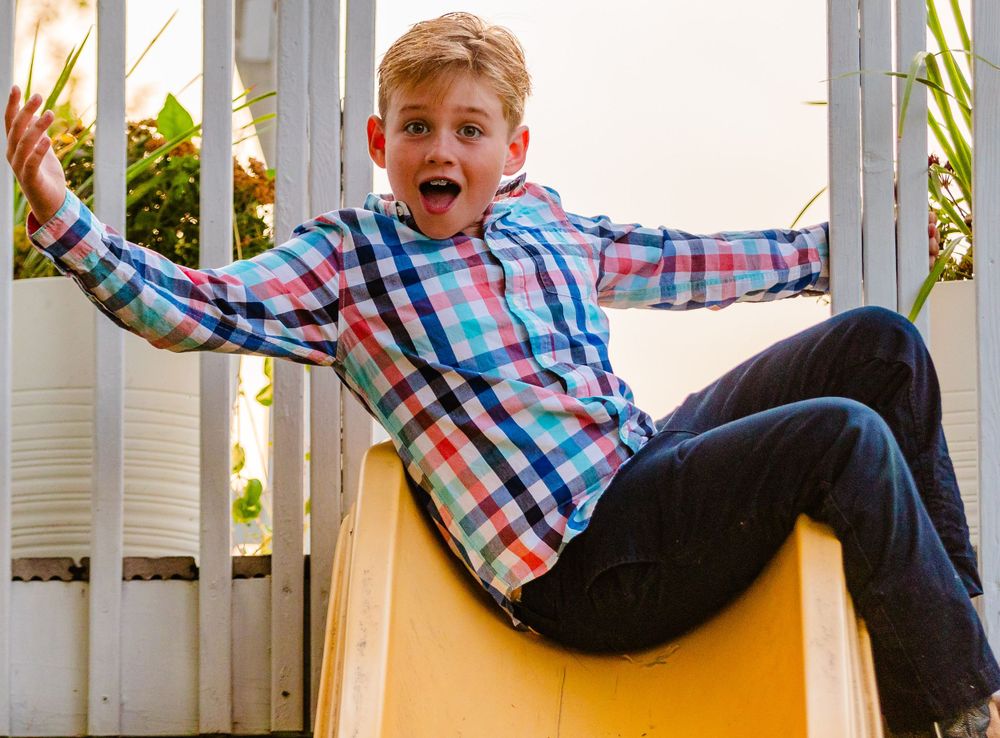 Child in plaid shirt slides down yellow playground slide with excited expression.