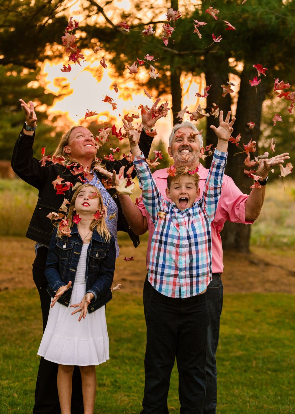 A group tossing pink flower petals in the air during golden hour sunset in a grassy outdoor setting.