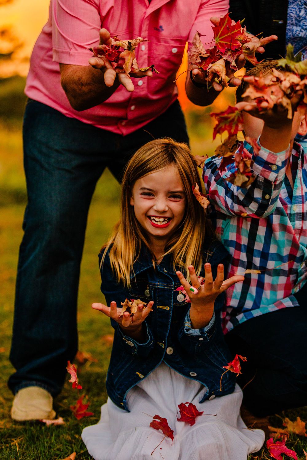 Playing with fallen autumn leaves in a garden while wearing denim and white tulle on a colorful fall day.