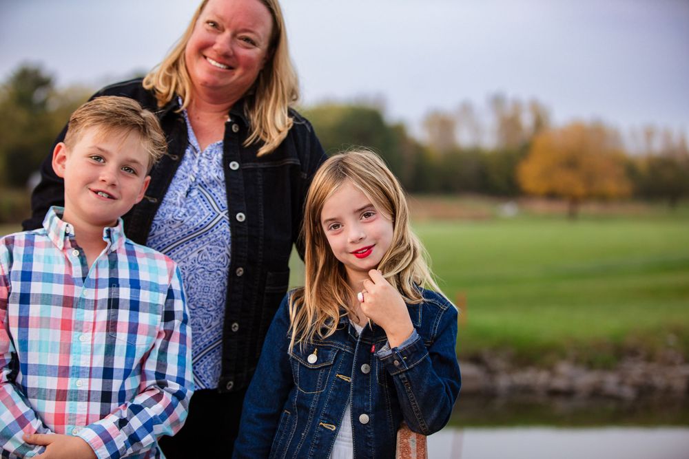 Family enjoying a warm autumn day outdoors with green fields and fall foliage in the background.