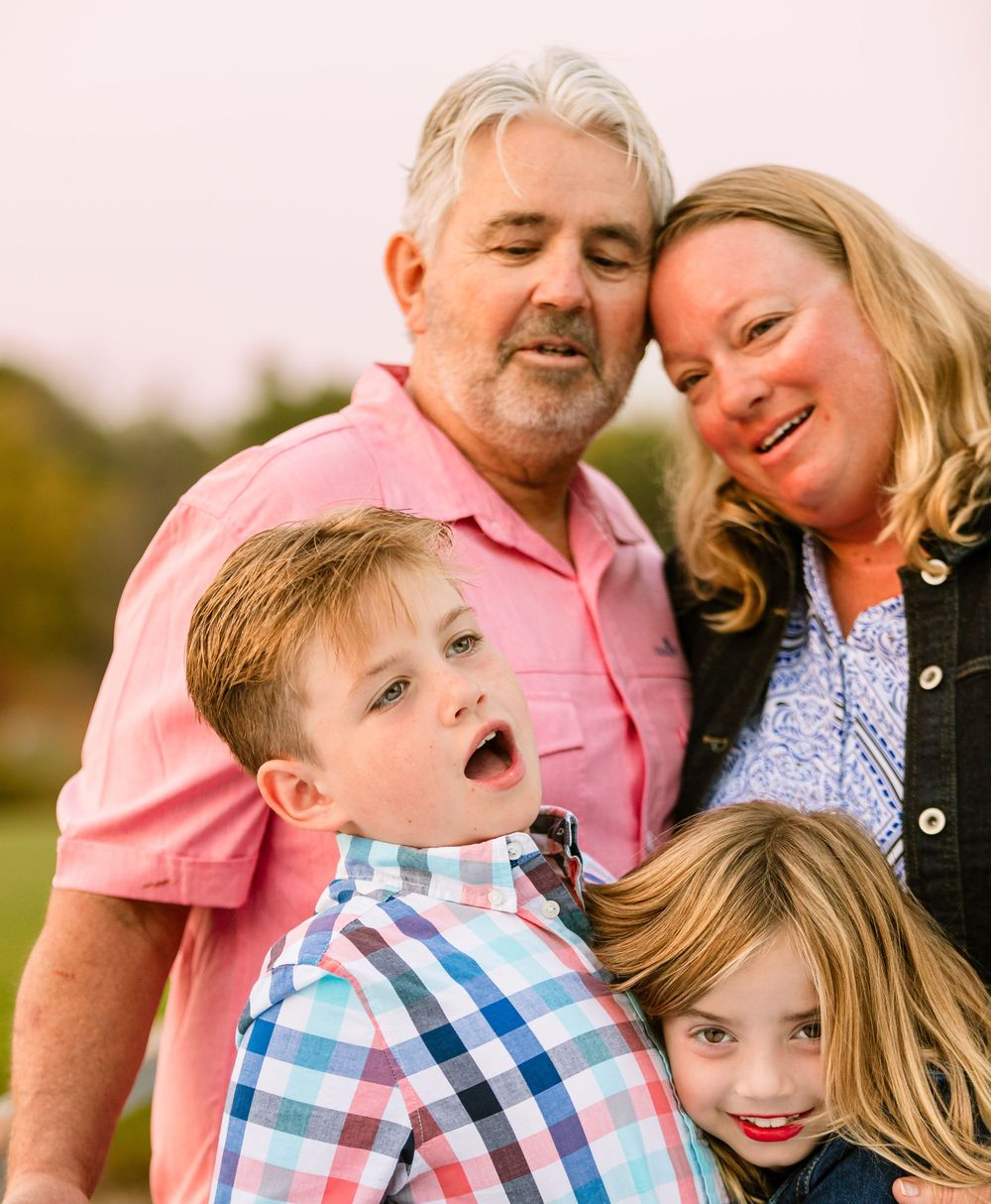 A happy family of four poses together outdoors with warm smiles during a photo session at sunset.