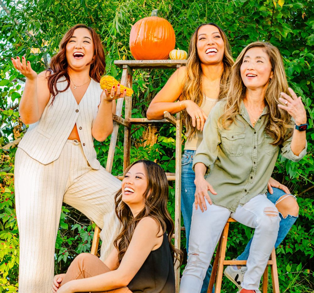 Festive fall photo with friends laughing together outdoors next to a wooden ladder decorated with a pumpkin.