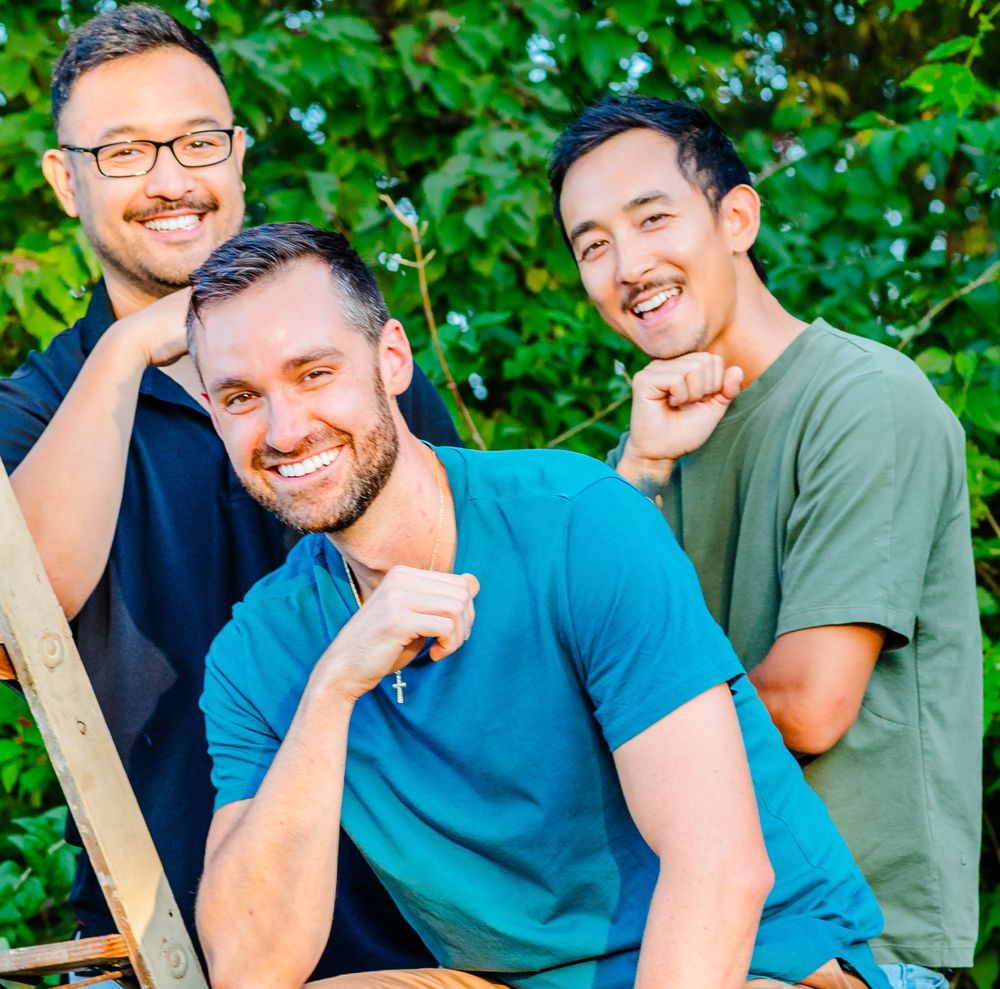 Three friends enjoying a casual outdoor gathering on a sunny day with green foliage in the background.