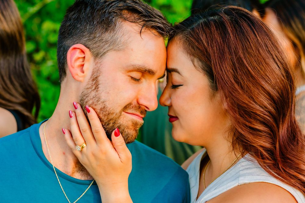 Two people share a tender romantic moment outdoors with lush greenery in the background.