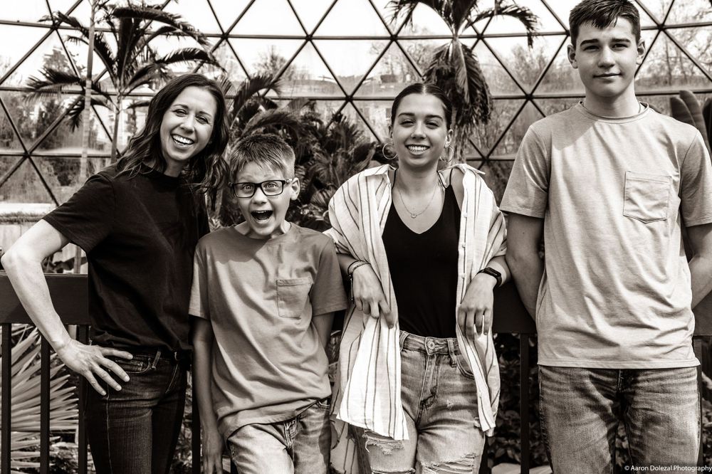 Black and white portrait of a happy family group of four standing together and smiling at the camera.