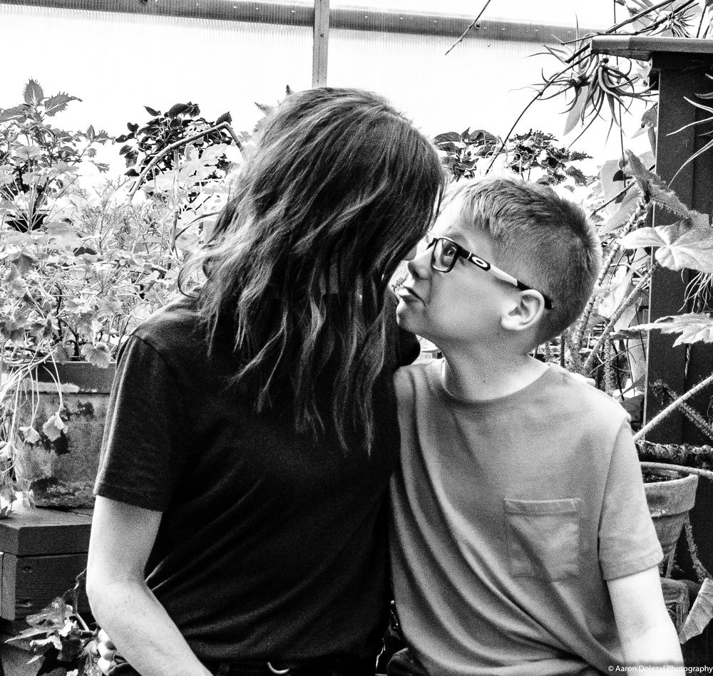 A tender moment between two people sitting together in a black and white photo surrounded by potted plants.