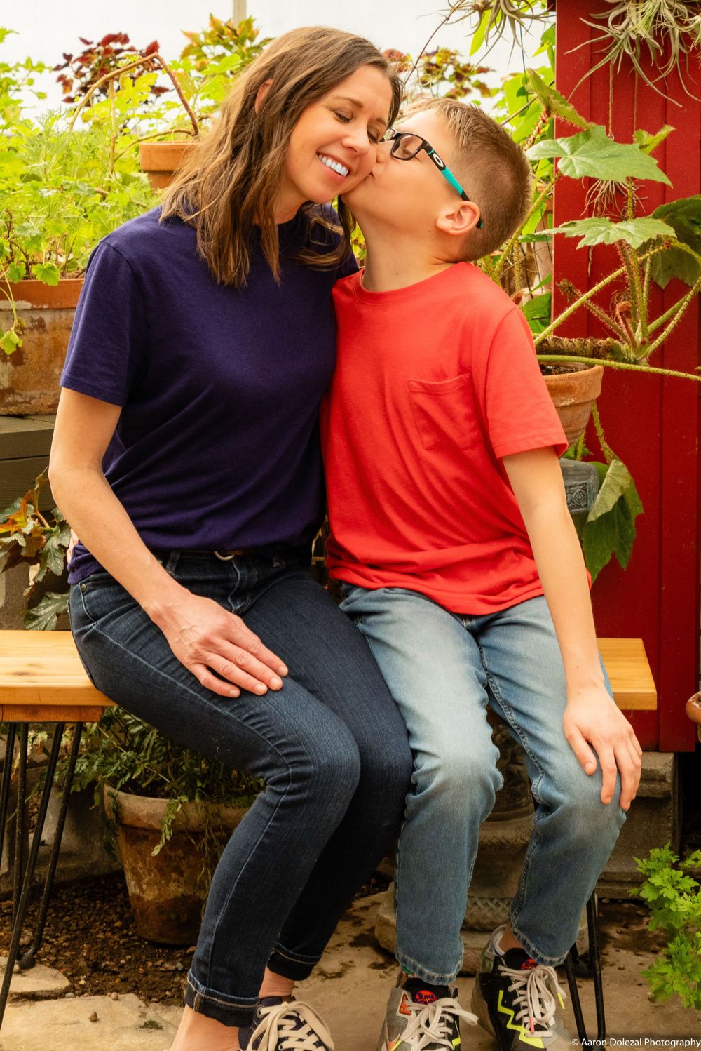 Sweet candid moment shared between parent and child sitting together on bench in garden with red barn wall behind them.