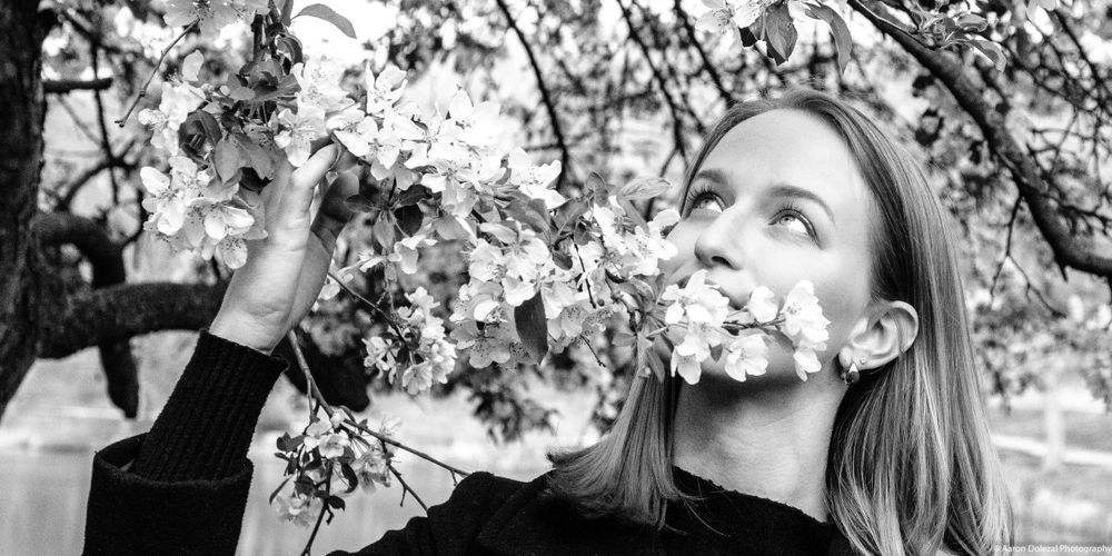 Black and white portrait of someone reaching up to touch cherry blossom branches.