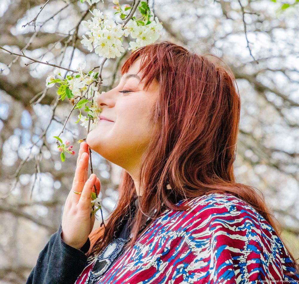 Person with vibrant patterned dress enjoying the fragrance of spring blossoms.