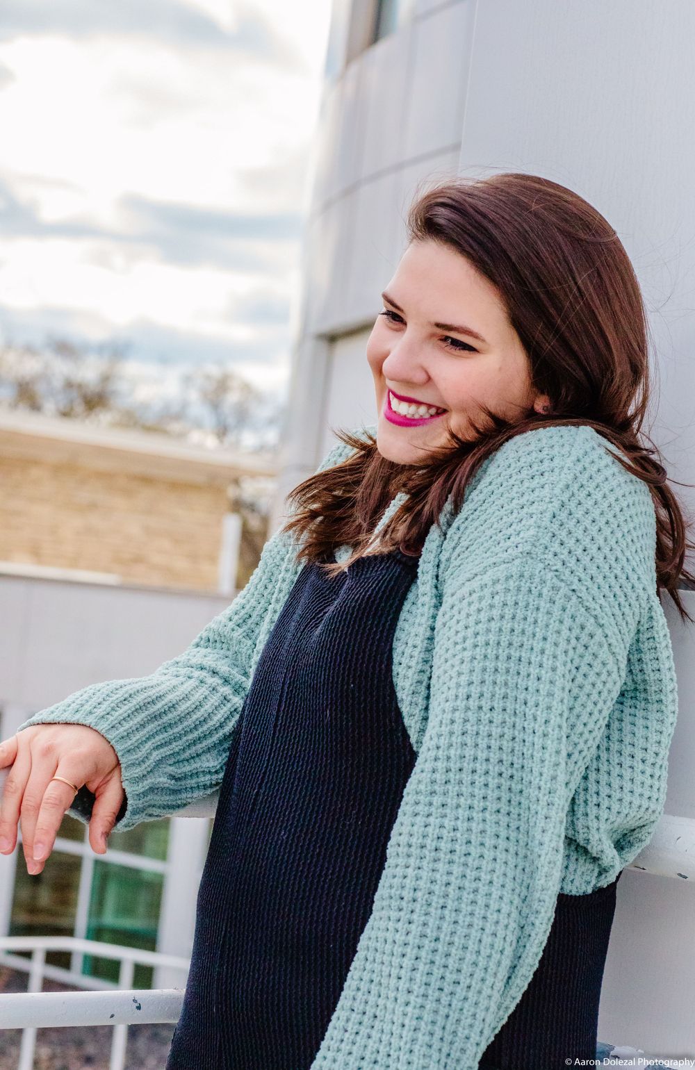 A person wearing a mint green knit cardigan over a navy top smiles while standing outdoors on a winter day.