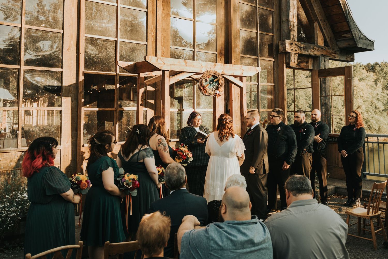 A wedding celebration taking place at a rustic glass venue with attendees in navy blue and white formal attire.