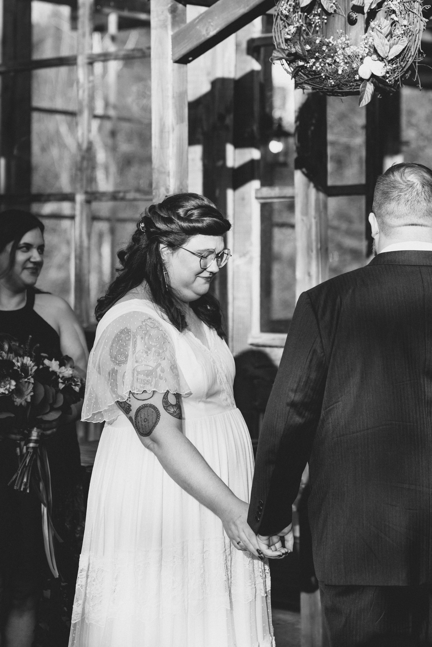 Black and white wedding ceremony moment showing a couple in vintage style dress holding hands.