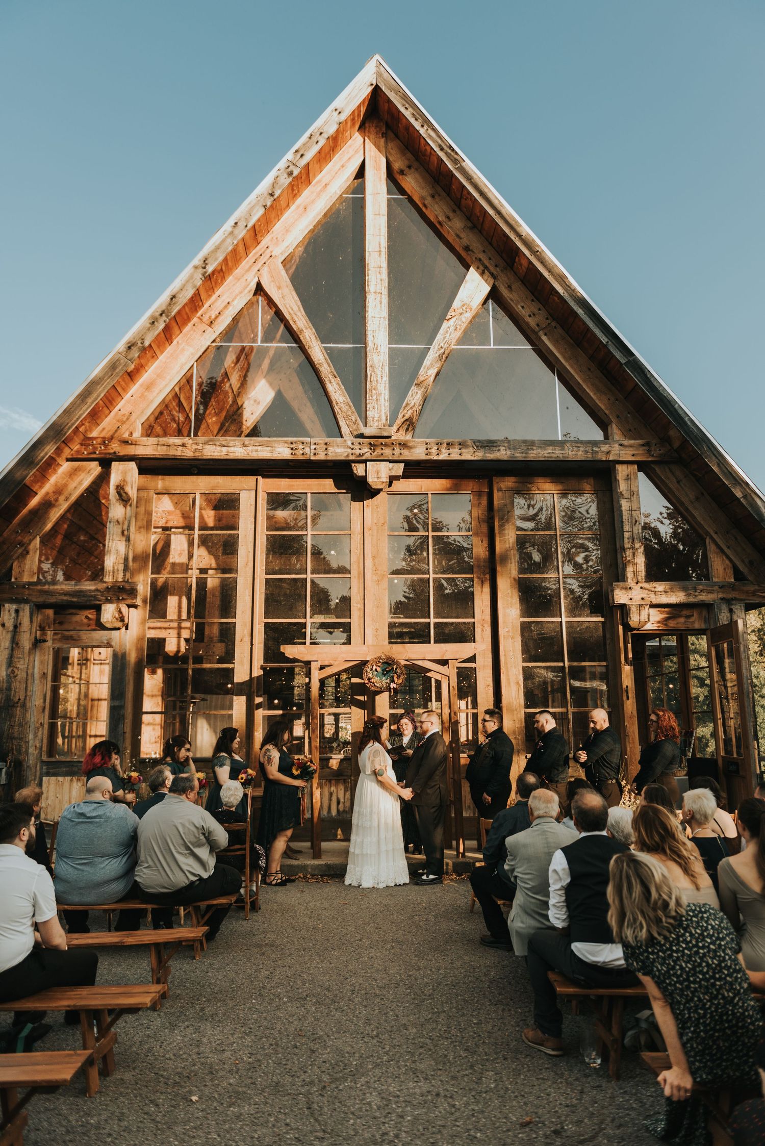 Wedding ceremony inside a rustic wooden chapel with exposed beams and glass windows at sunset.