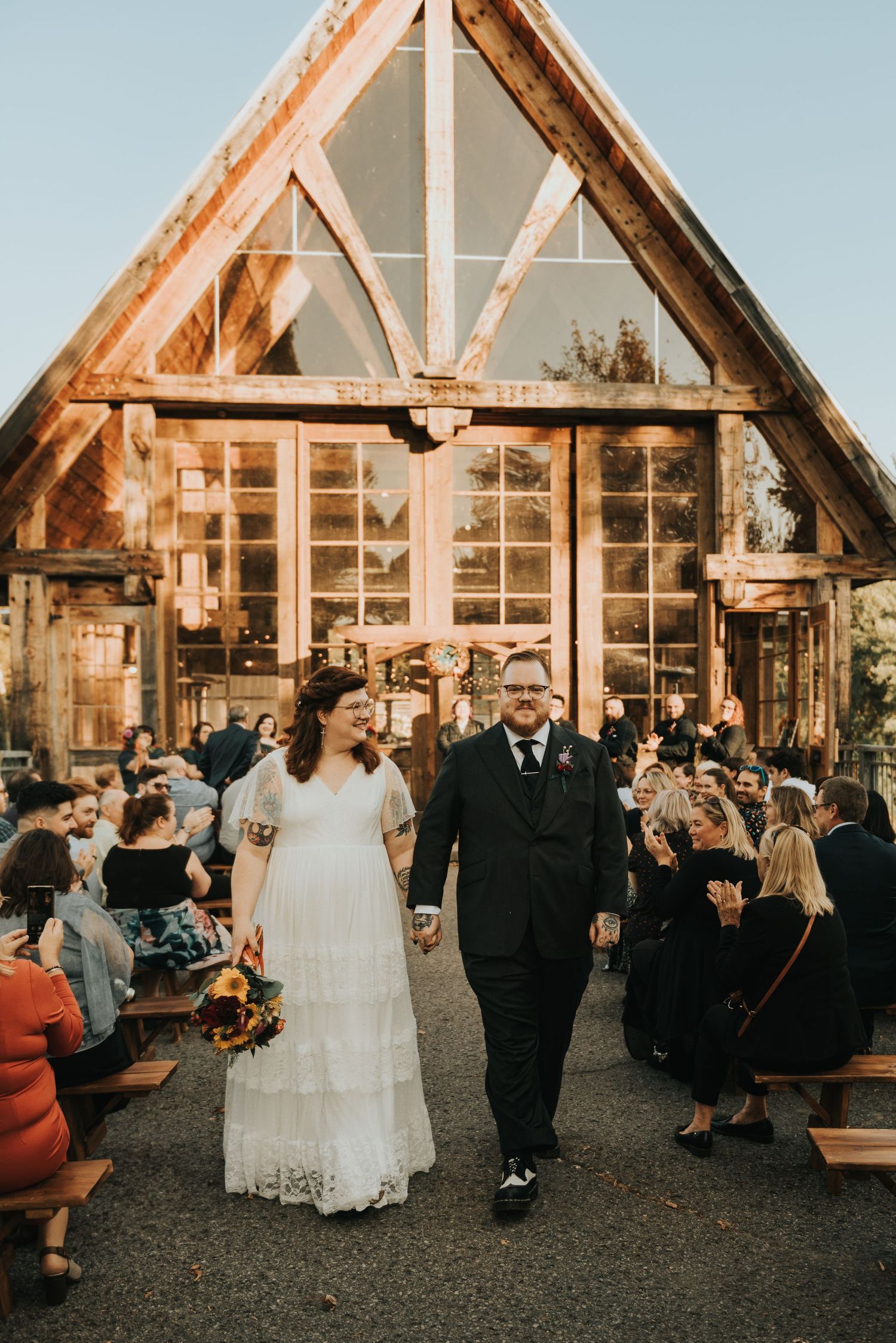 A rustic wooden chapel serves as backdrop while newlyweds exit through rows of guests on their wedding day.
