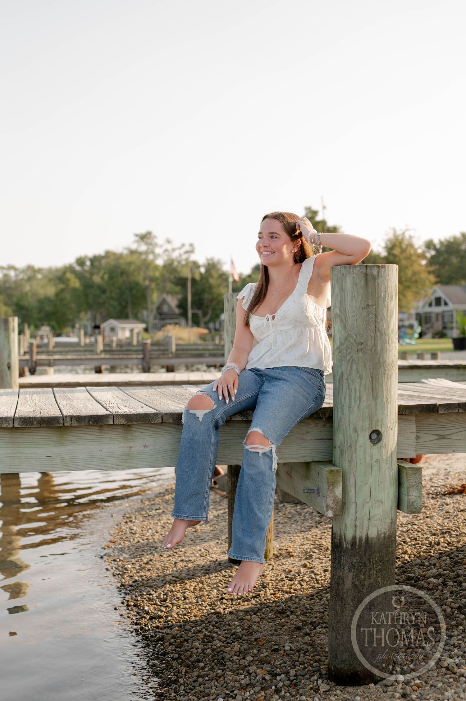 Casual summer portrait of someone sitting on a dock piling wearing ripped jeans.