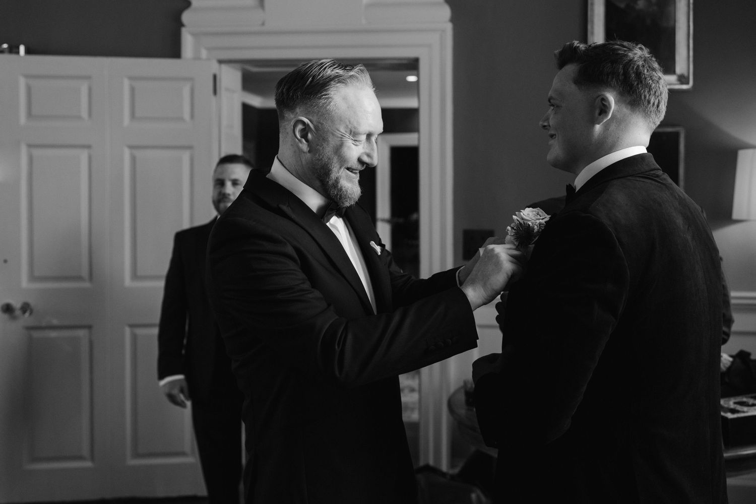 groomsmen helping groom with boutonniere in library at iscoyd park