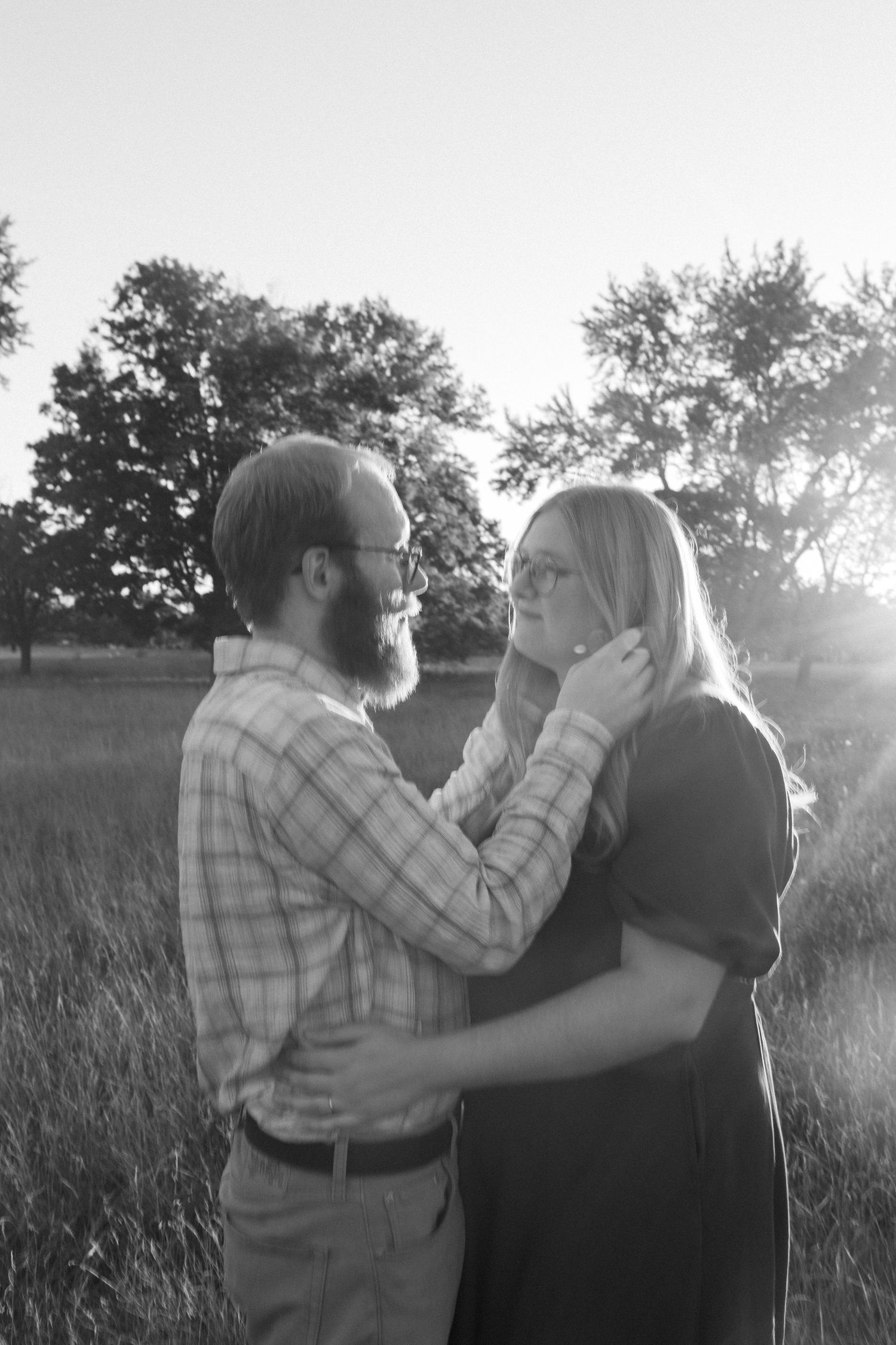 A couple shares an intimate moment together in a sunlit field with trees silhouetted in the background.