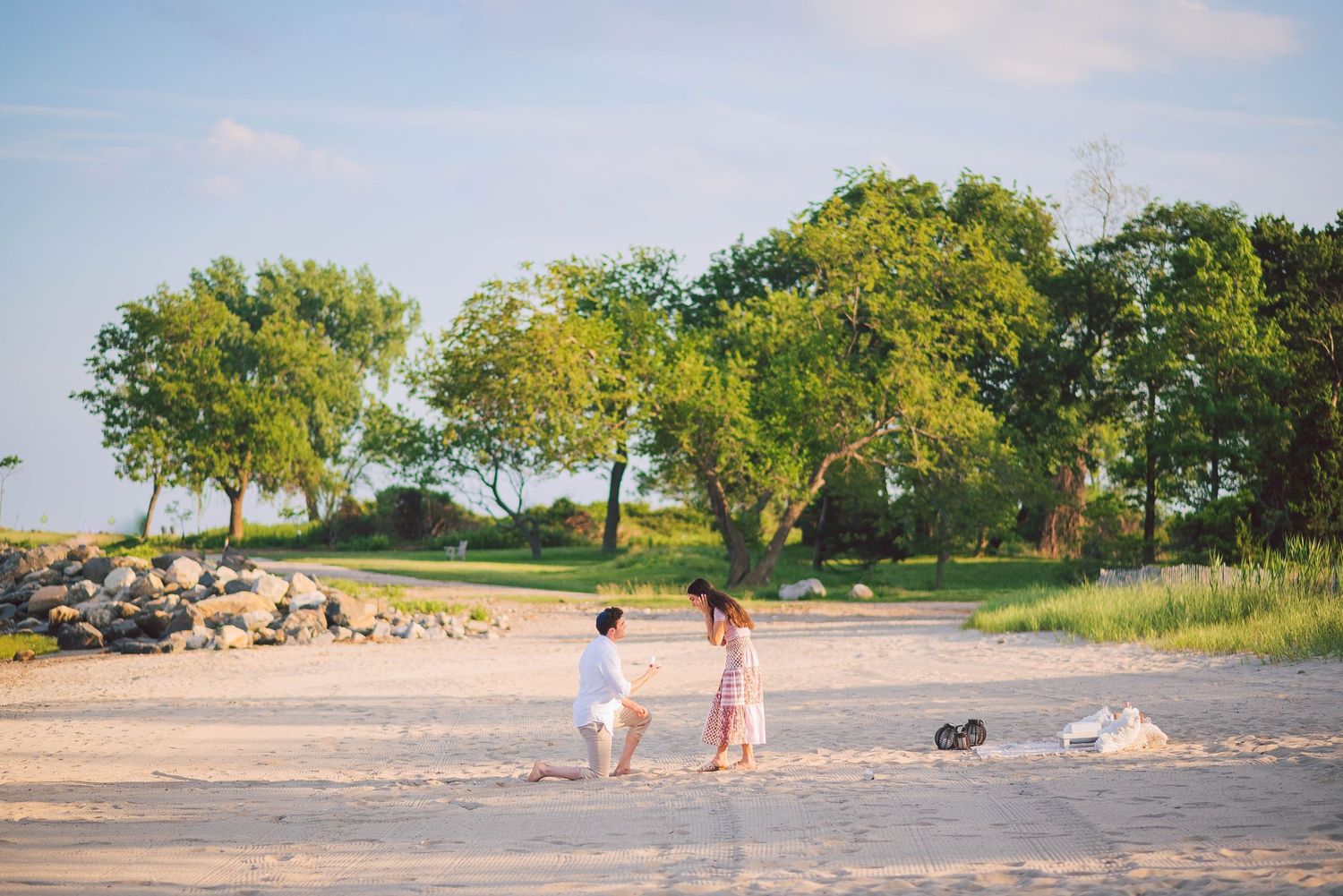 Wide panoramic view of a sandy beach with trees and natural landscape in the background.