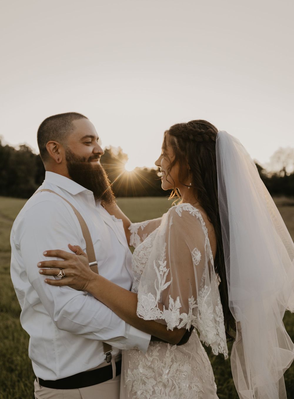 Bride and groom sharing a joyful moment embracing in a field during a beautiful golden sunset.