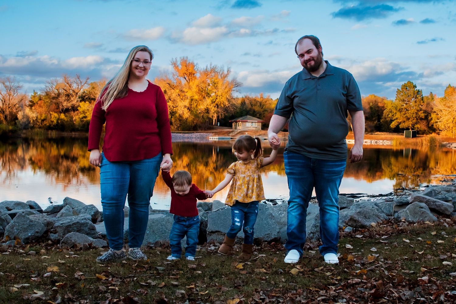 Family standing together by a scenic autumn lake with golden foliage in the background.