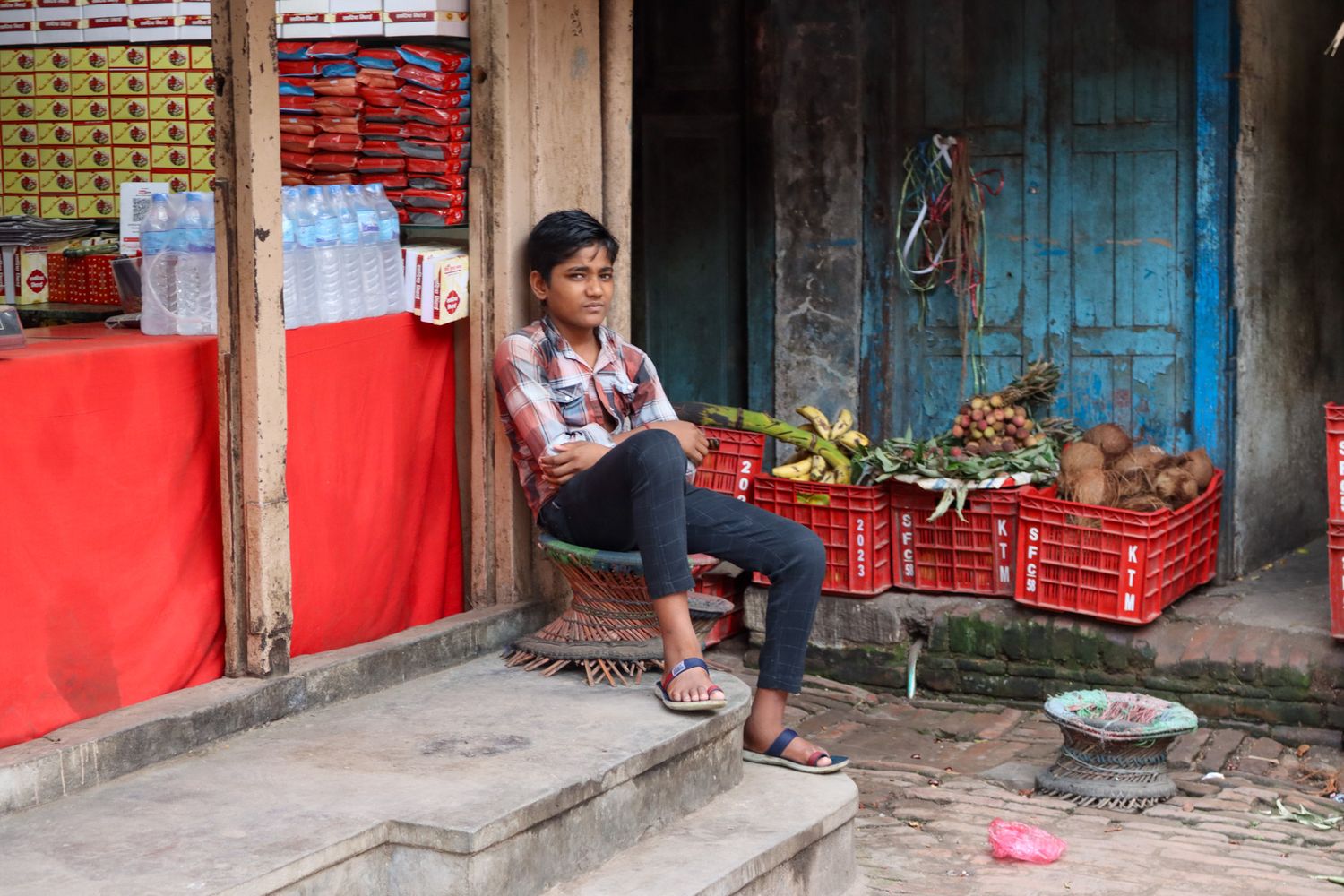 street portraiture in Bhaktapur, Kathmandu. Boy sitting outside grocery shop. 
Nepal street life captured during travel by Emma Drohan