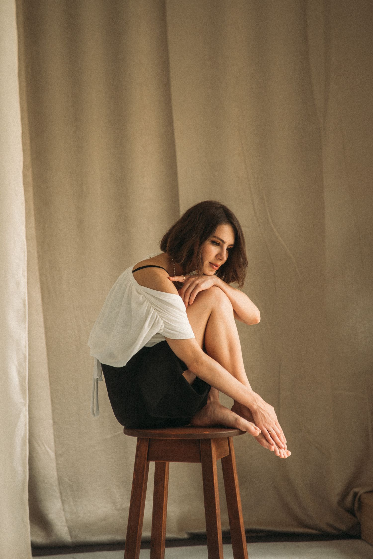 Minimalist portrait series featuring soft poses on wooden stool against neutral backdrop.