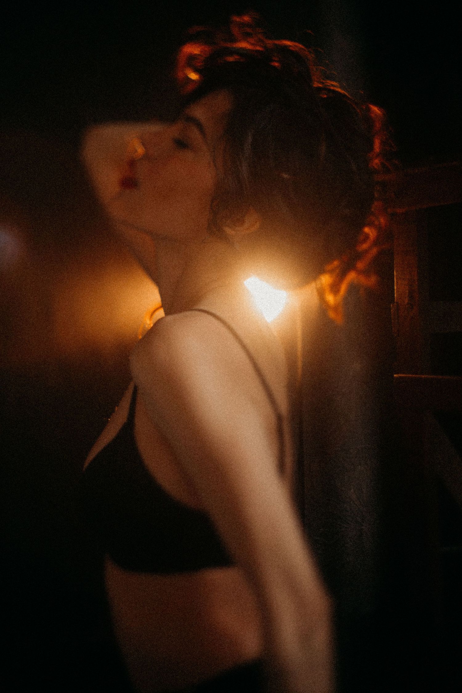 Intimate low-key portrait with warm backlighting creating dramatic shadows and highlights.