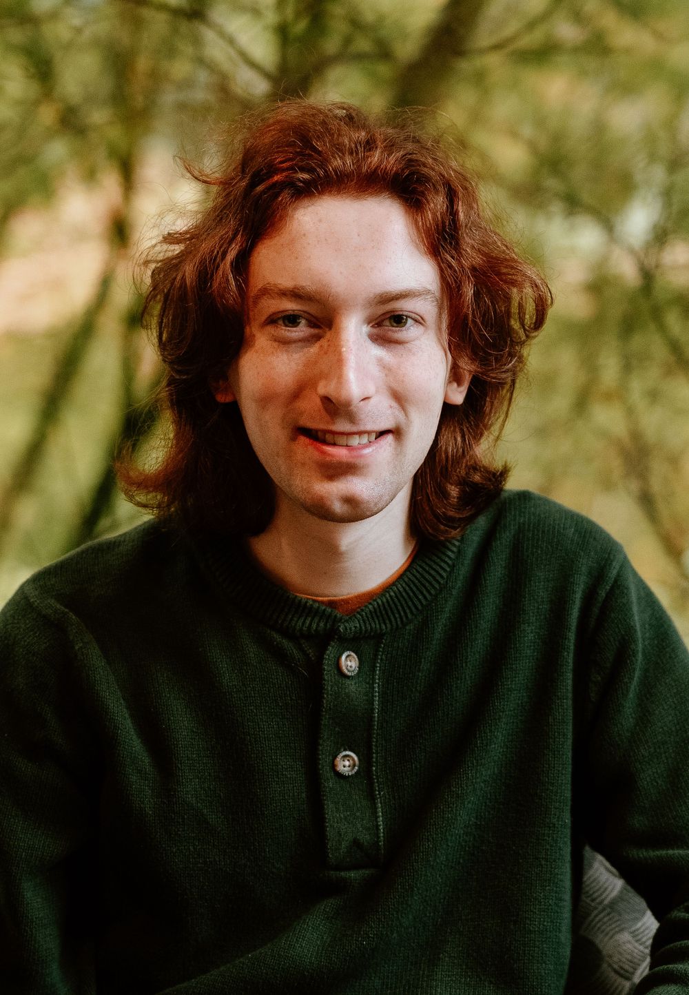 Outdoor portrait of someone in a green henley sweater with natural background.